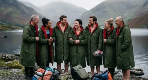A diverse group of British outdoor swimmers wearing matching green changing robes for wild swimming together by a cold freshwater lake.