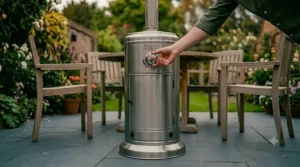 A man's hand turning the control dial on the front panel of a stainless steel mushroom patio heater to ignite it.