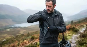 Mountain biker taking a break on a chilly Scottish trail, adjusting the zip vents on their heated cycling jacket.