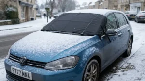 Snow resting on top of a frost-free heated windscreen cover on a small hatchback