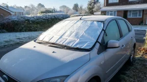 Reflective heated windscreen covers glistening under low winter morning sunlight on a parked hatchback